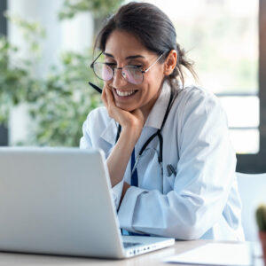 Shot of smiling female doctor working with her laptop in the consultation.