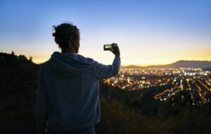 Chile, Santiago, woman taking cell phone picture in the mountains above the city at sunset