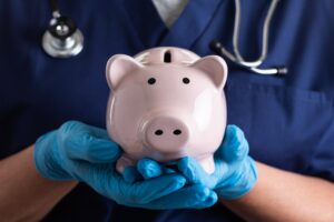 Doctor or Nurse Wearing Surgical Gloves Holding Piggy Bank